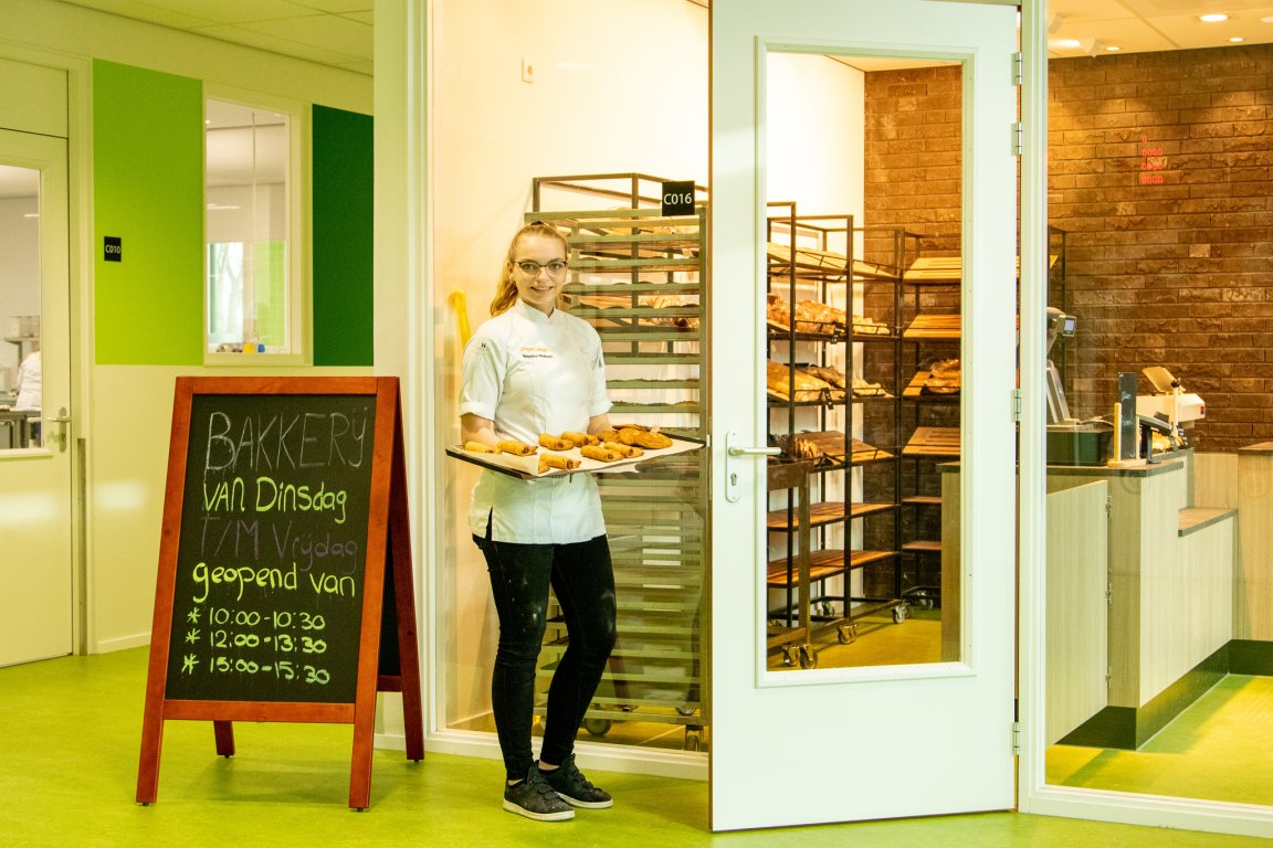 Een student brood en banket met een schaal broodjes voor de schoolbakkerij